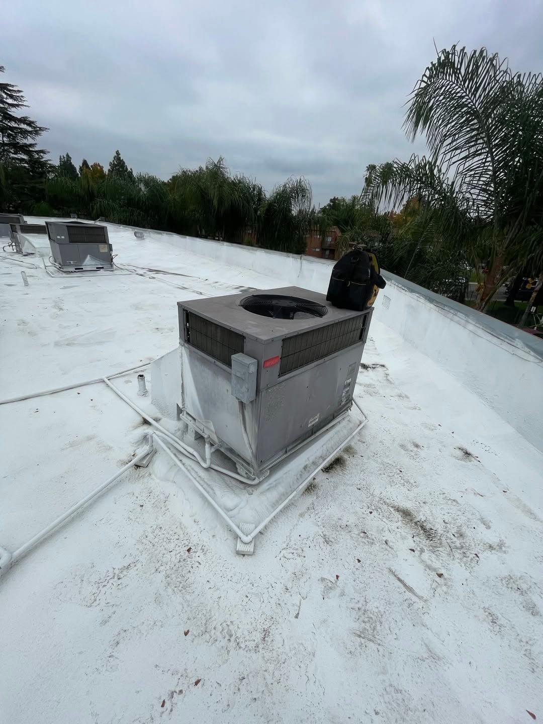 Rooftop HVAC unit on a white flat roof under cloudy skies, with trees in the background