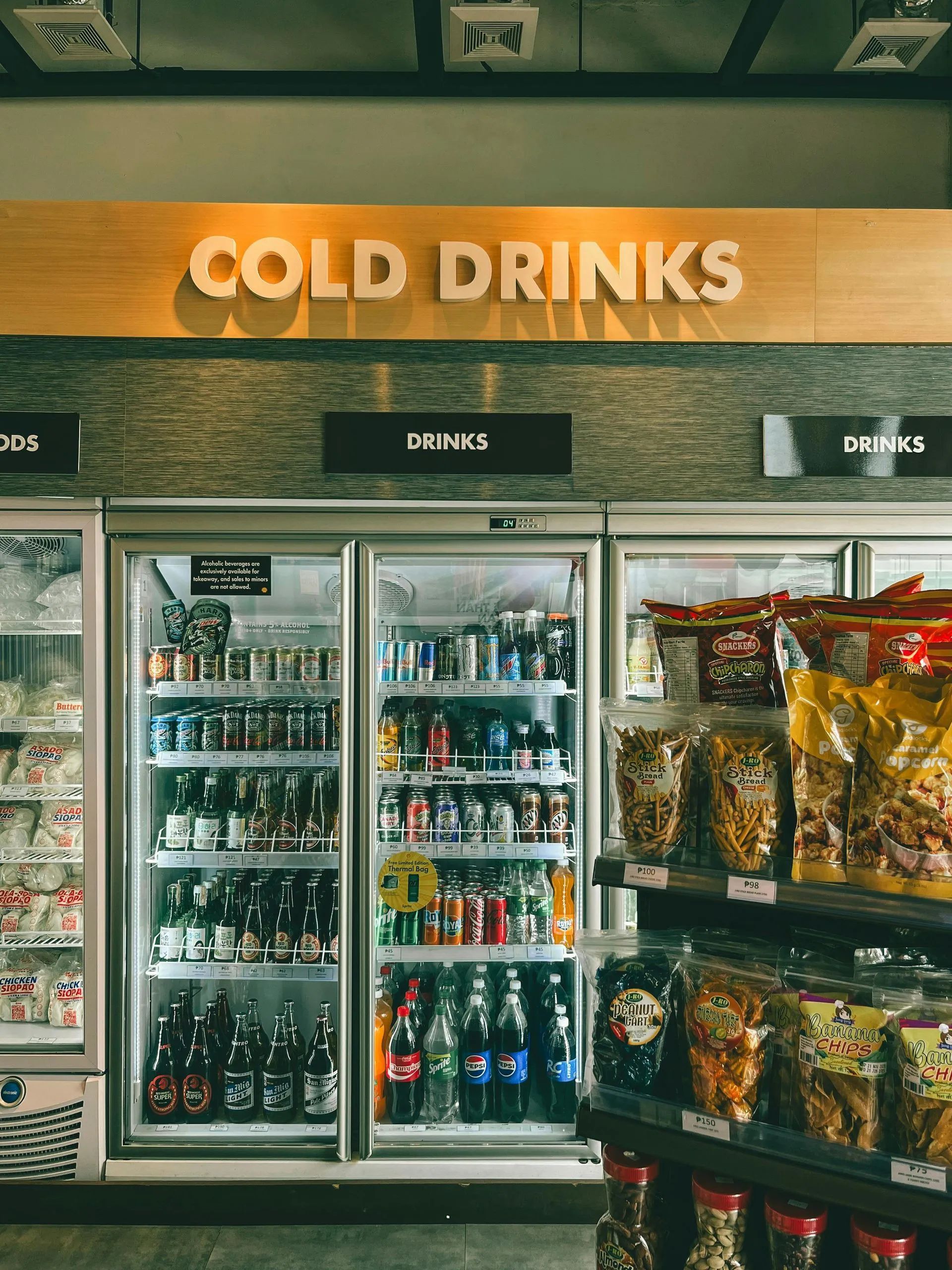 Convenience store cold drinks cooler with glass doors and snacks displayed on the right