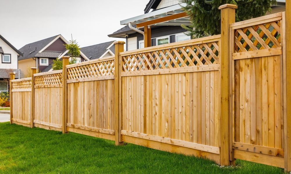 A wooden fence surrounds a lush green lawn in front of a house.