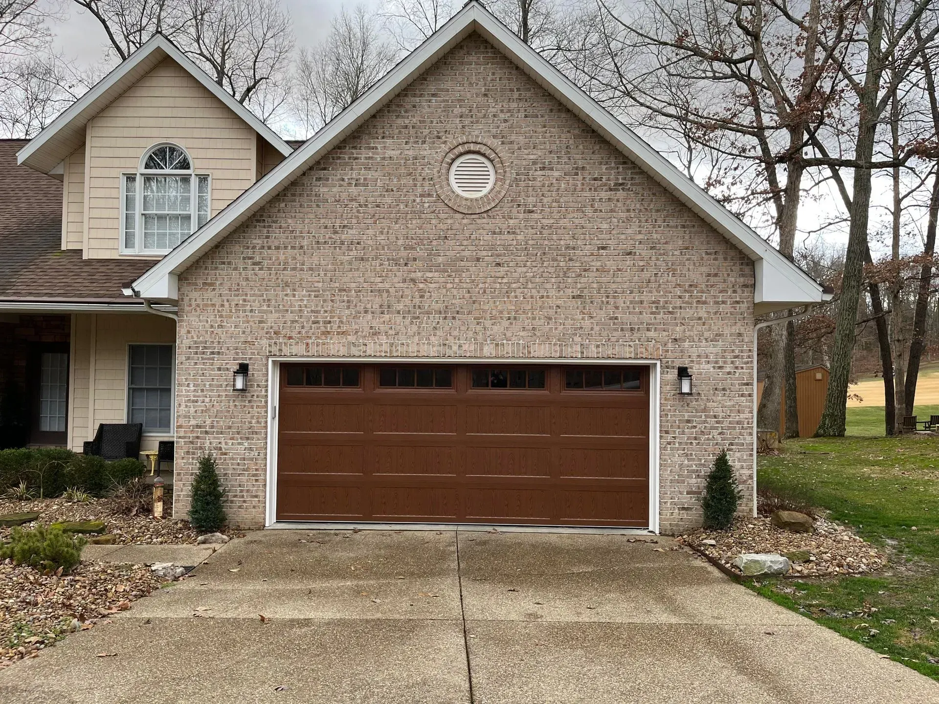 Suburban house with tan siding and a brown garage door, viewed from the driveway.