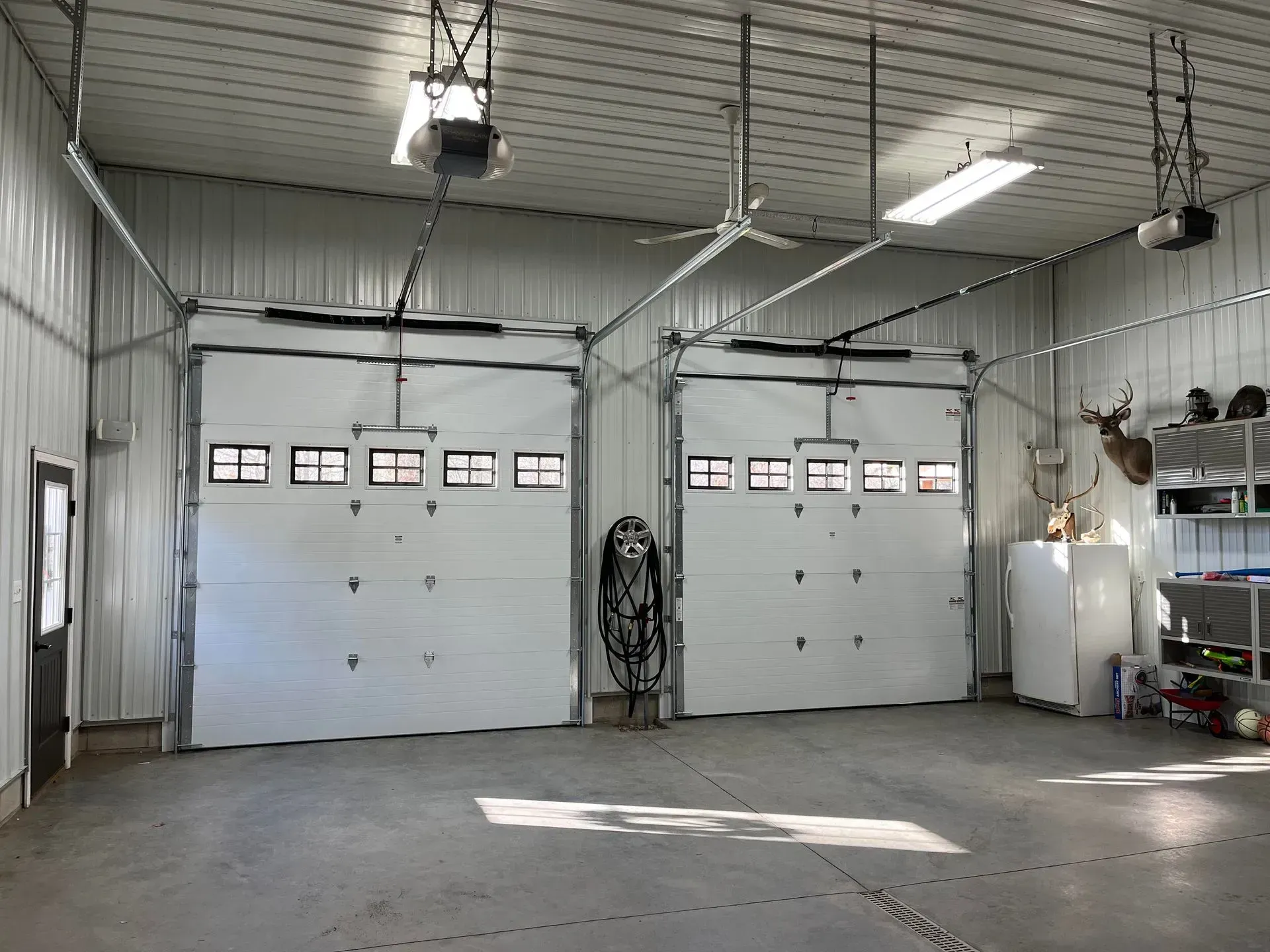 Empty white garage with two large doors, overhead lights, and a concrete floor.