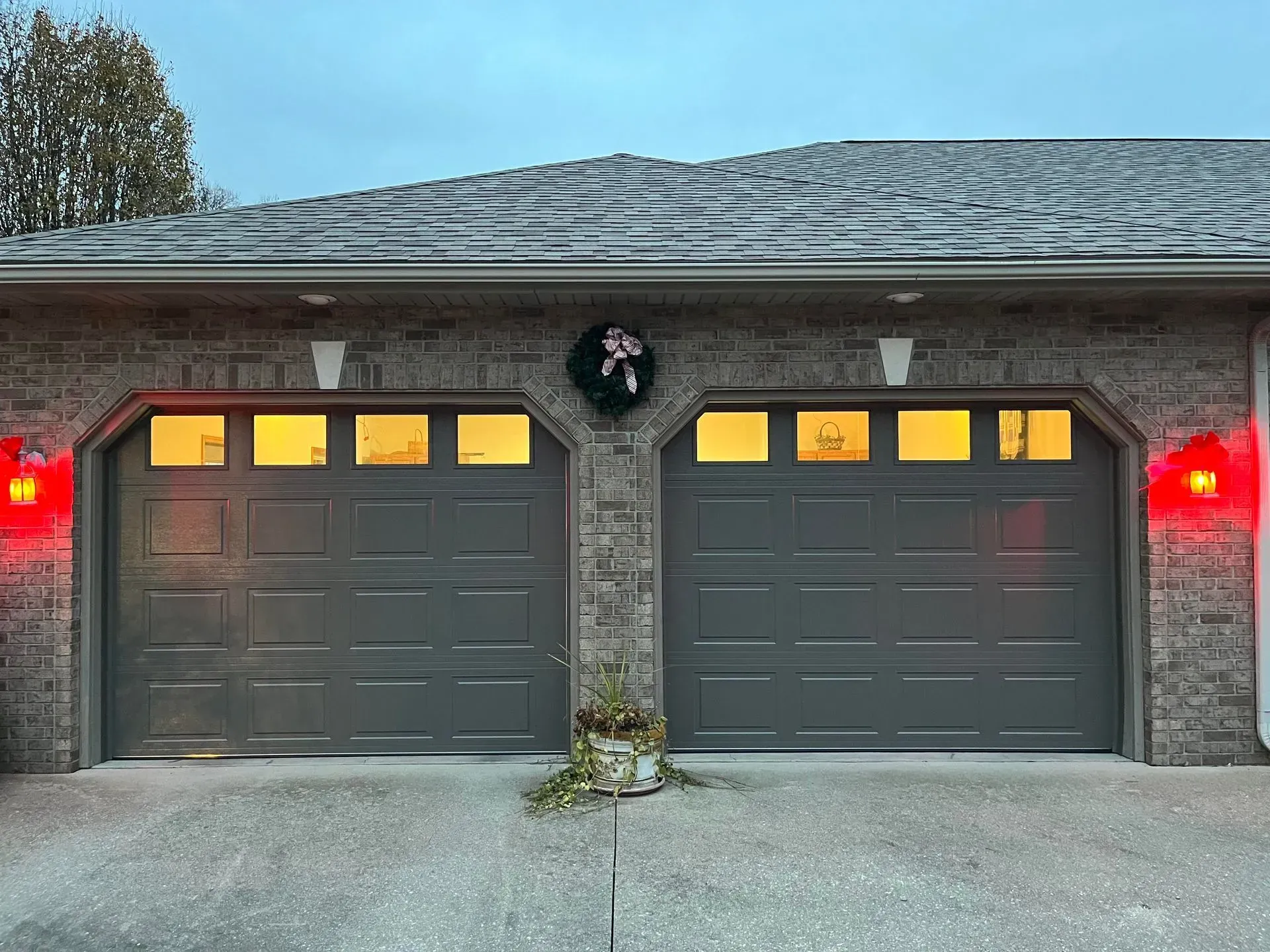 Two-car gray garage with lit windows, red exterior lights, and a wreath above the center pillar