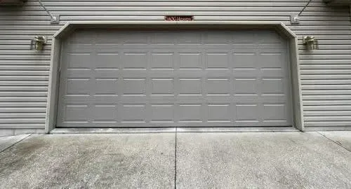 Closed gray garage door on a beige house with a concrete driveway in front