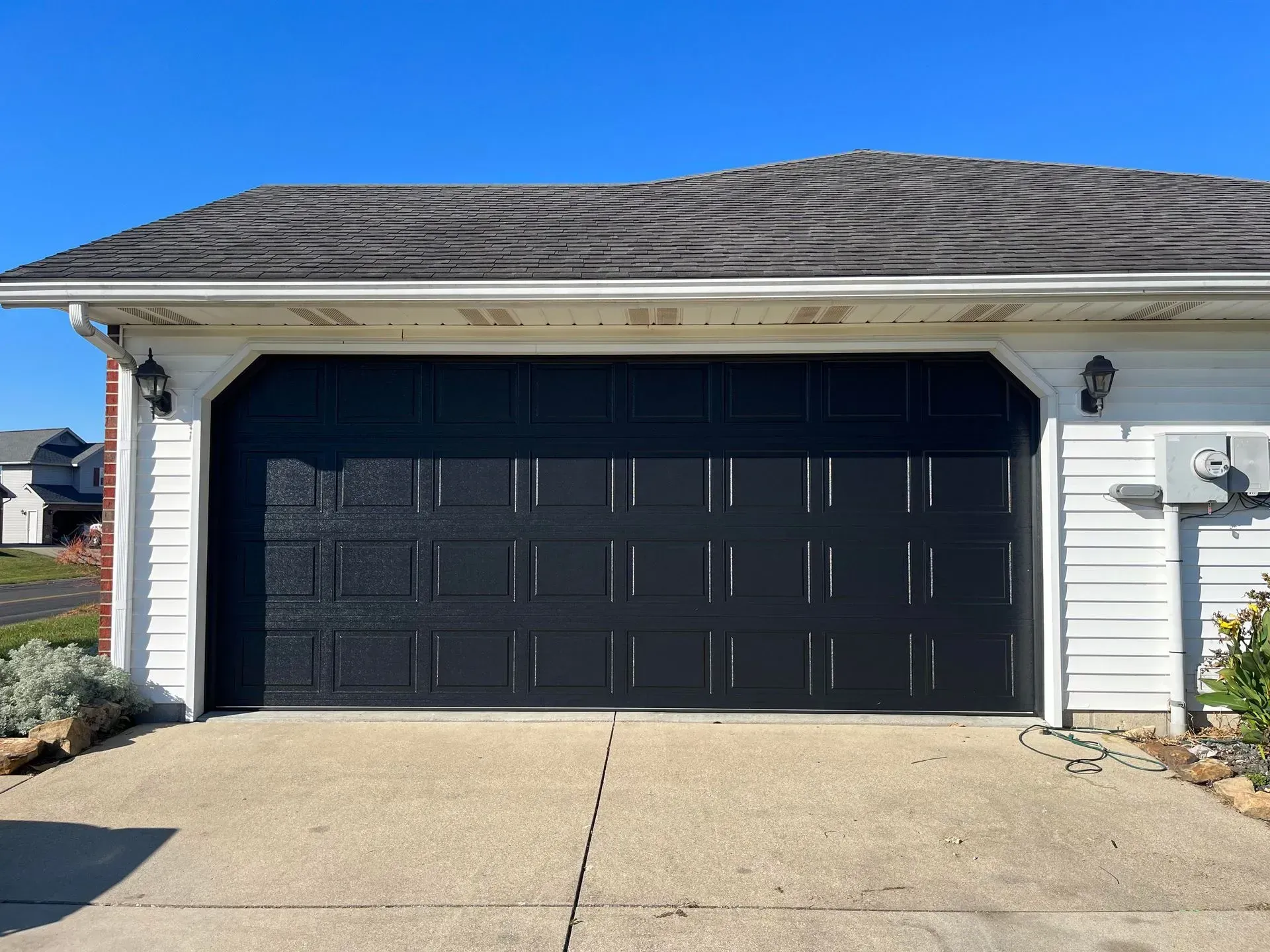 Black two-car garage door on a white suburban house with a concrete driveway under a blue sky