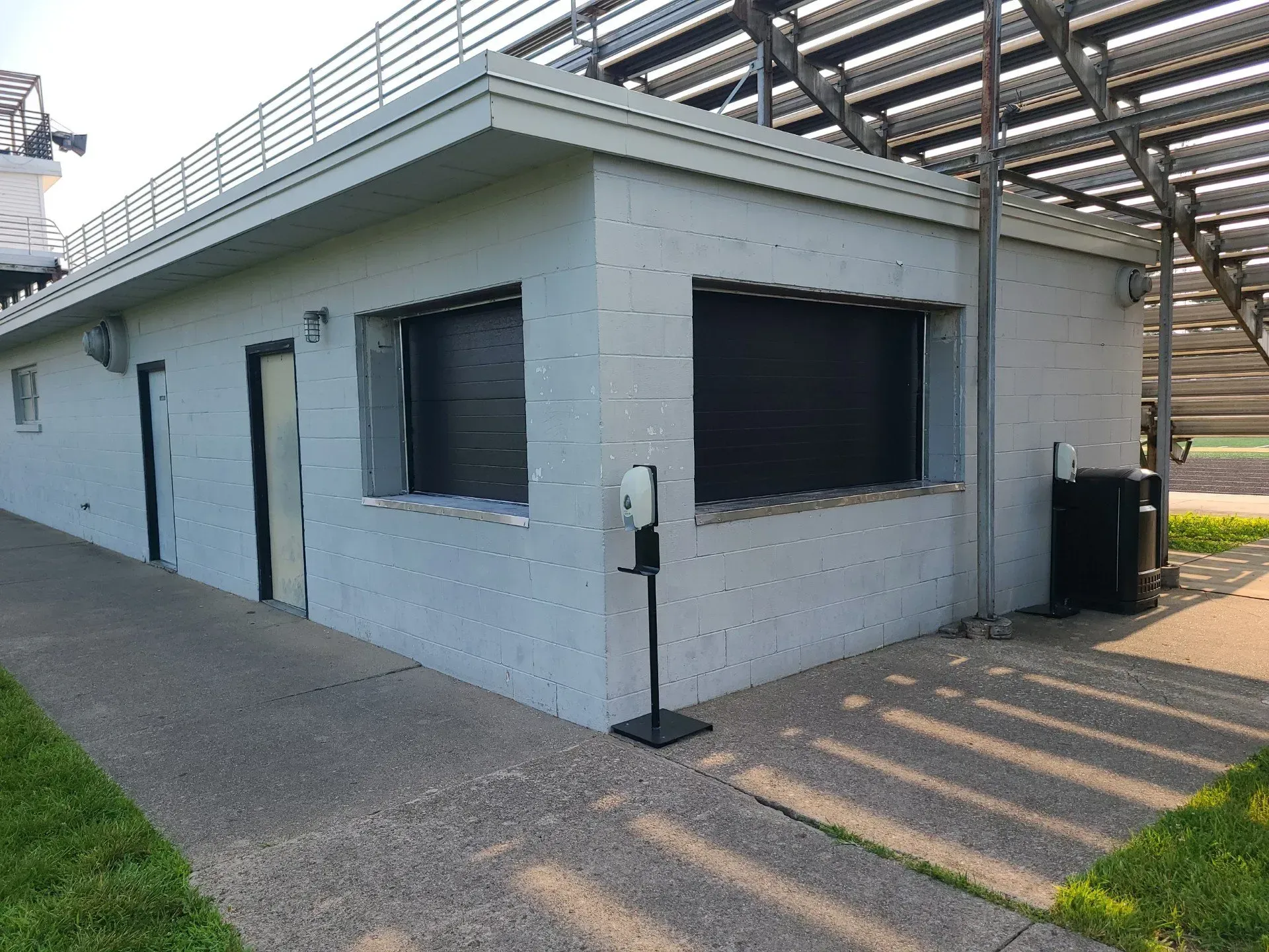 Small gray building with dark windows, a side door, and a walkway under a metal canopy