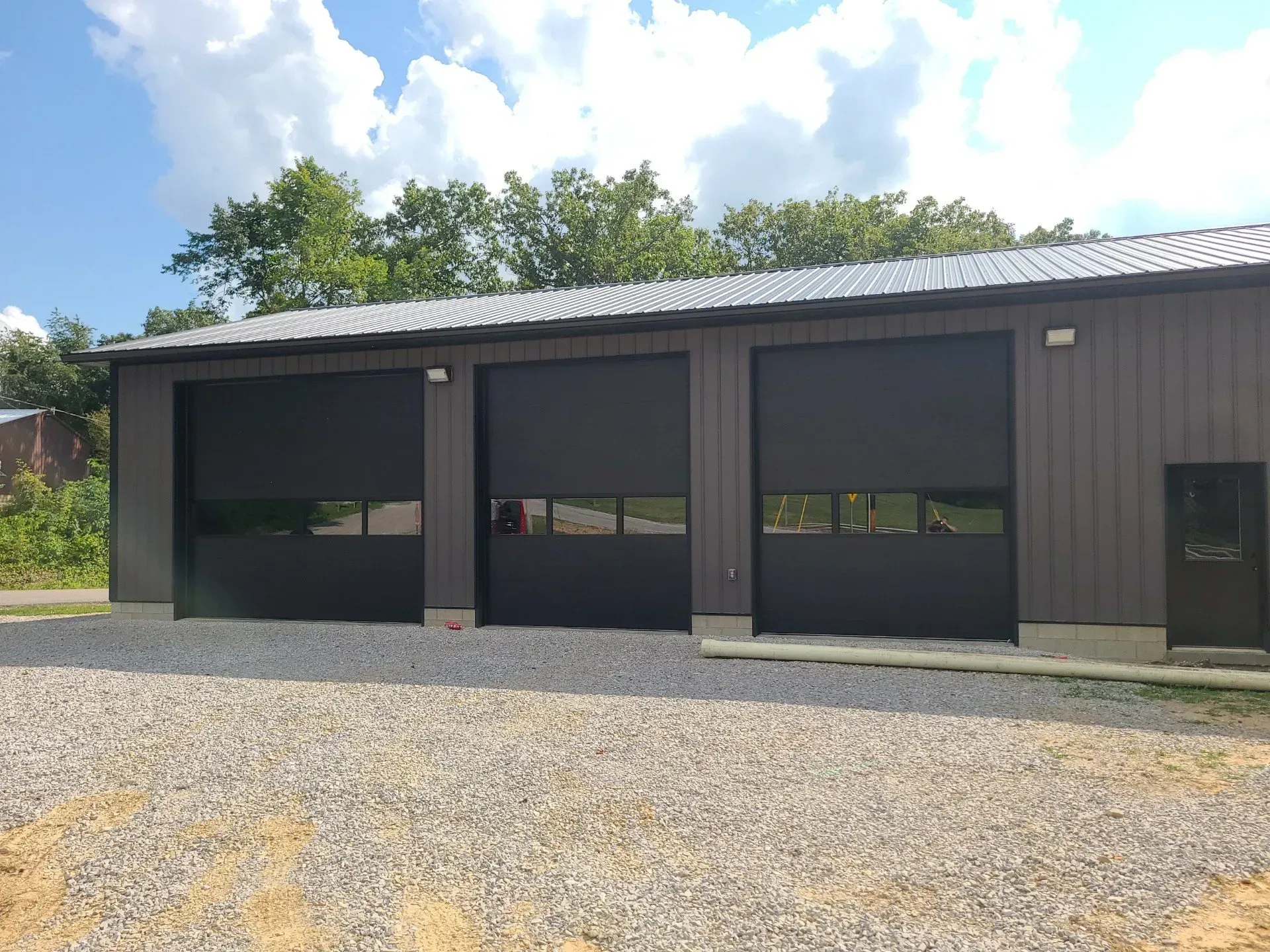 Dark gray garage or workshop building with large doors and gravel foreground under a blue sky