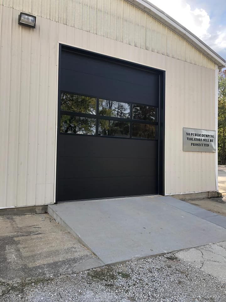 Industrial building with a large black garage door and a concrete ramp entrance