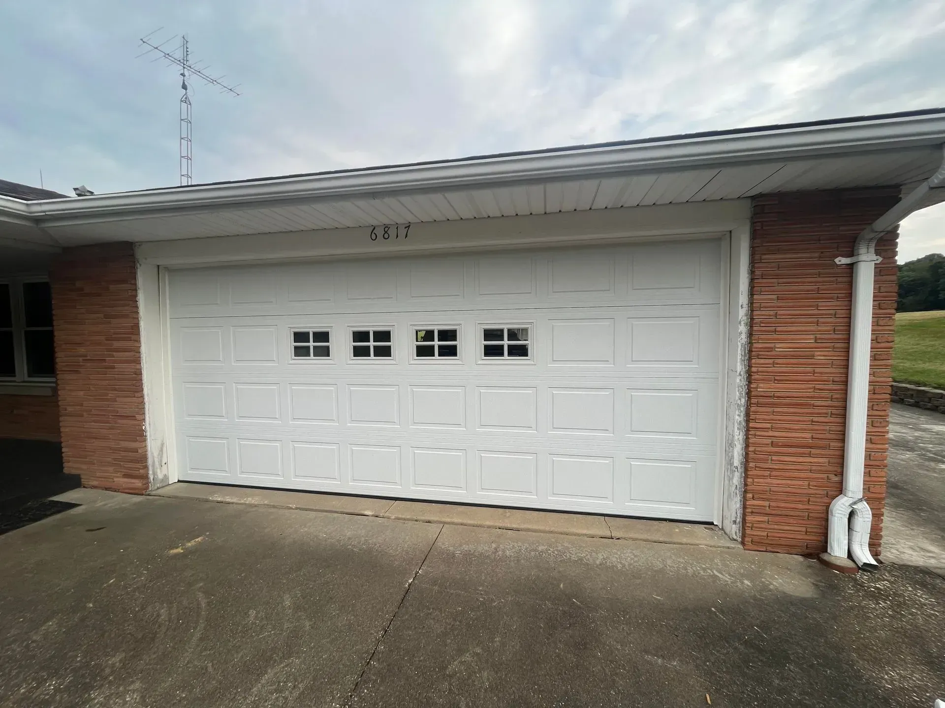 White garage door on a brick house with a concrete driveway and cloudy sky.