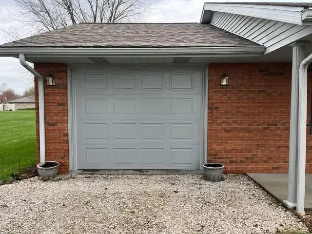 Gray garage door on a brick house with gravel driveway and two potted plants