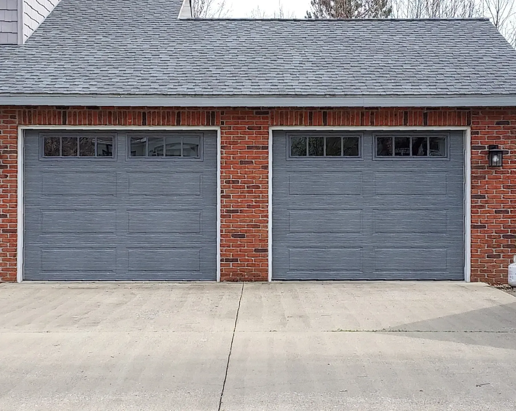 Two gray garage doors on a red brick building with a concrete driveway