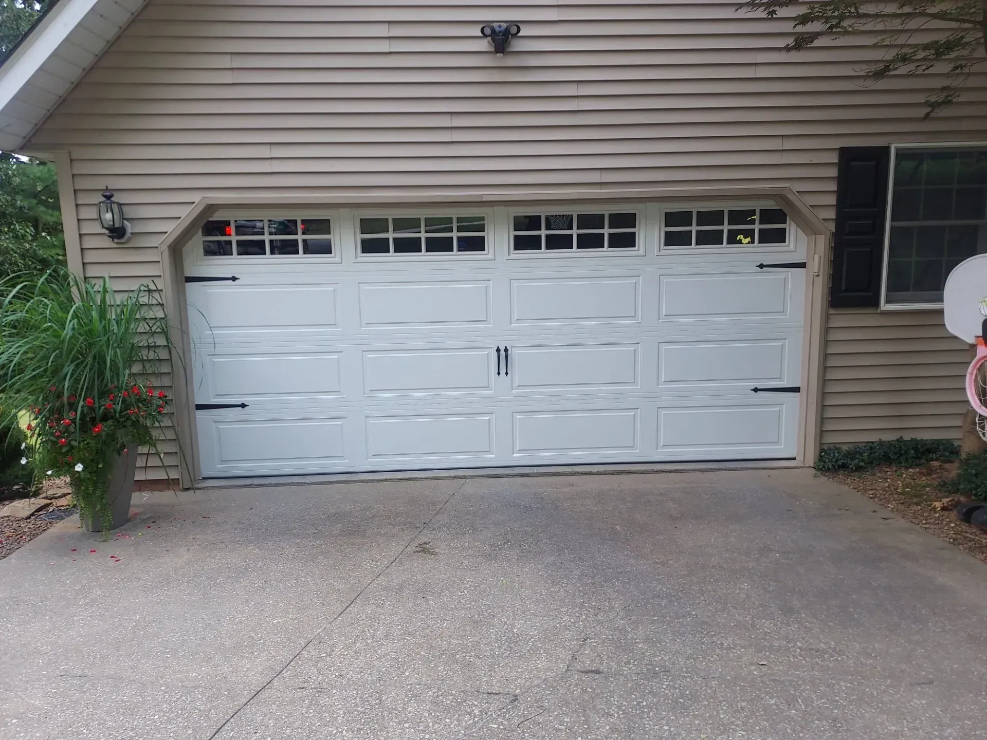 White double garage door on a beige house with a concrete driveway and shrubs on either side