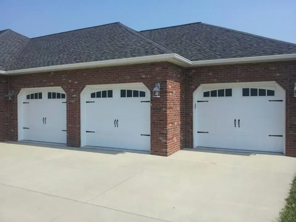 Three white garage doors on a red brick house with a gray shingled roof and concrete driveway