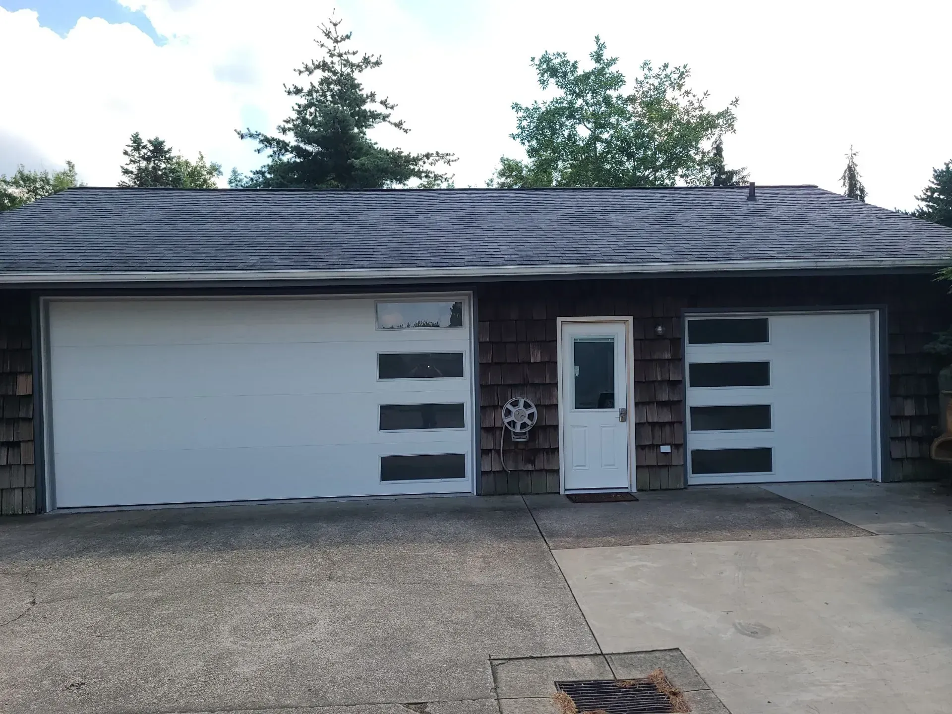 Two-car garage with white doors and a central entry door under a dark shingled roof.