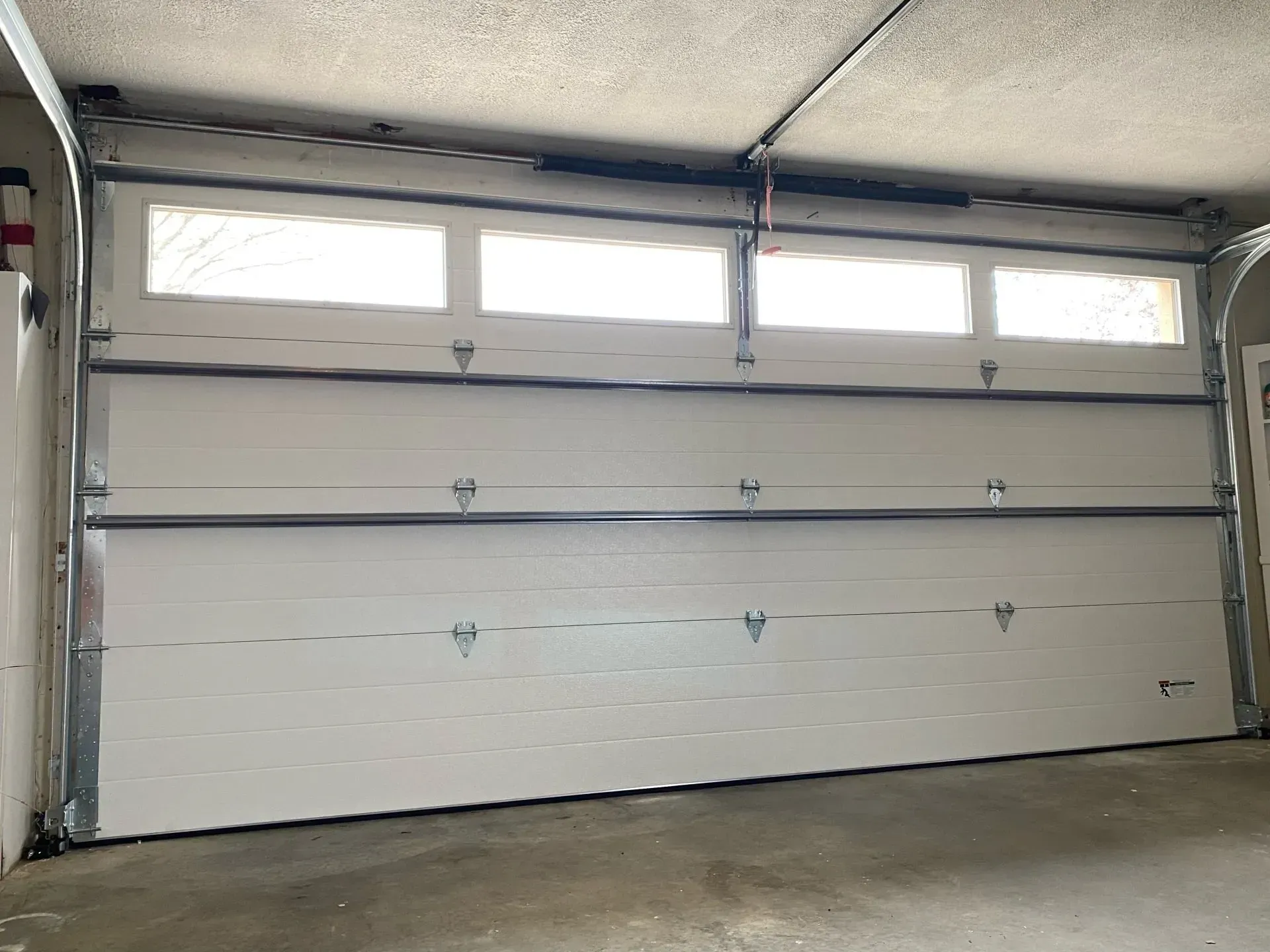 White garage door with windows at the top inside a concrete garage.