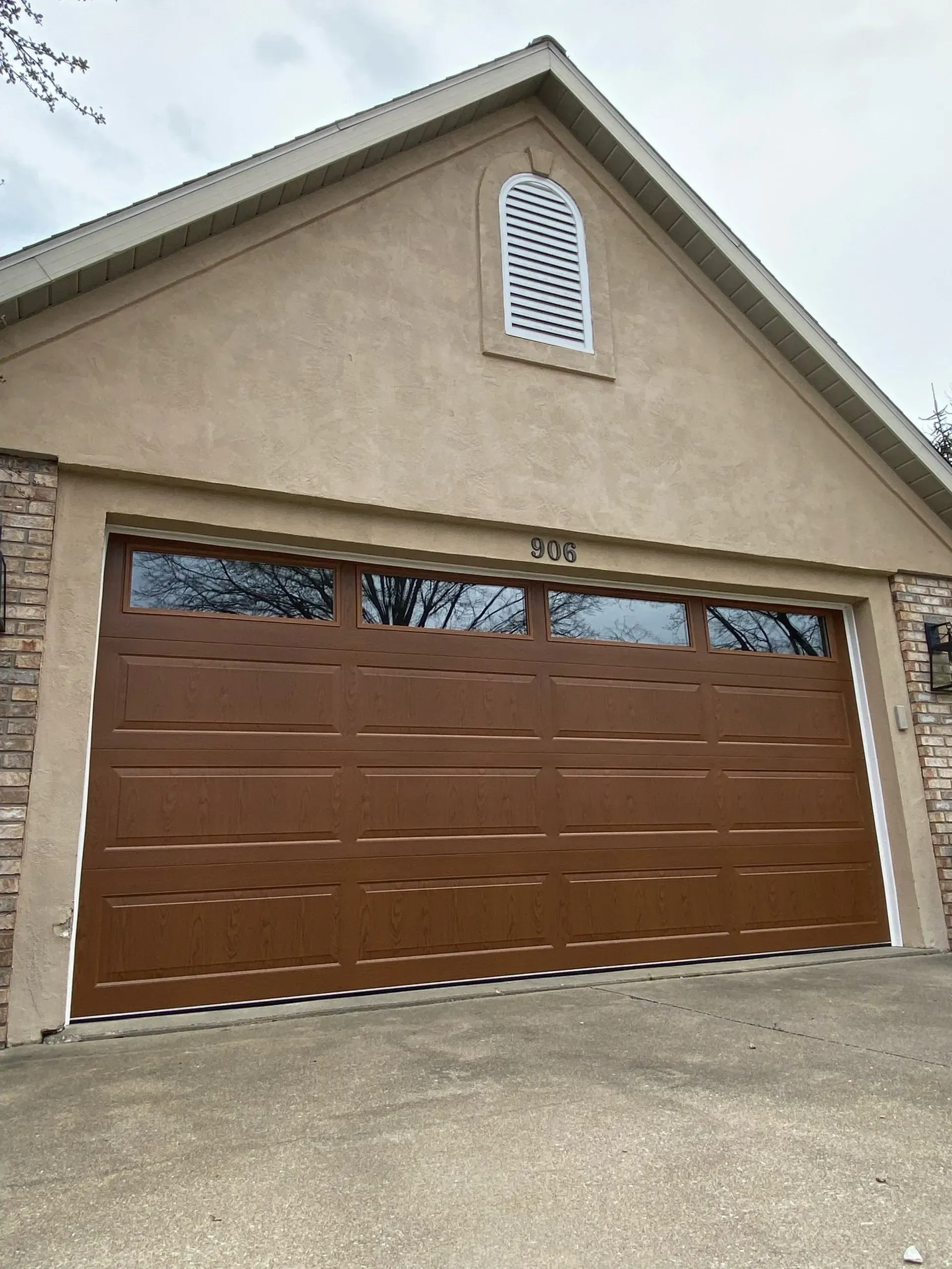 Beige house exterior with a brown garage door and decorative arched window above.