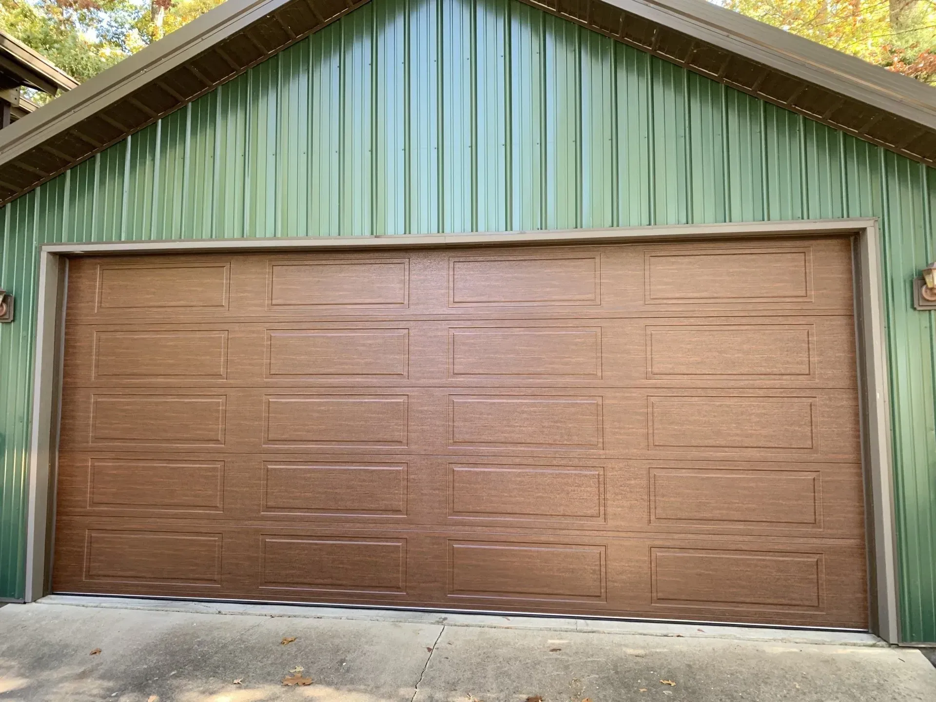 Brown garage door on a green-sided building with a peaked roof, viewed from the driveway