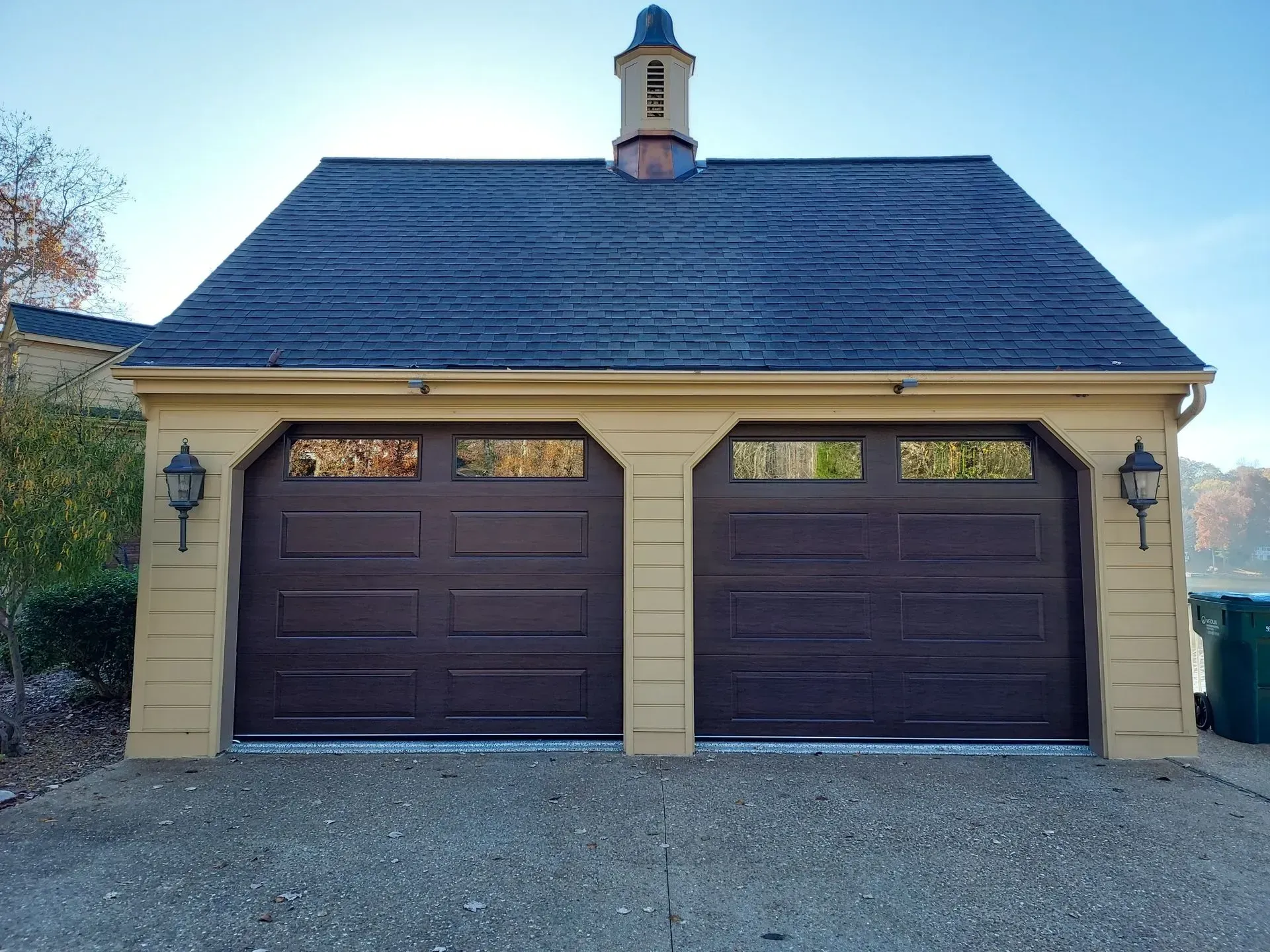 Two-car garage with dark brown doors, beige siding, and a gray shingled roof.