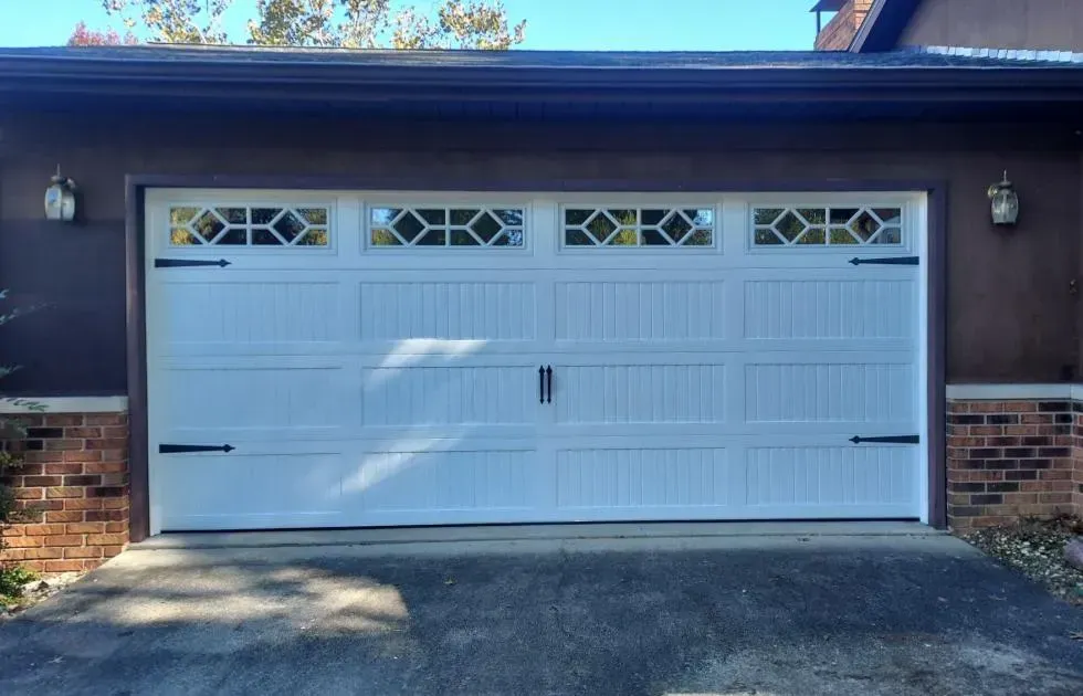White double garage door with small decorative windows, set in a dark brick house facade.