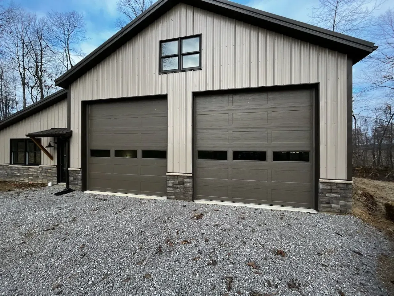 Tan metal garage with two large doors and gravel driveway
