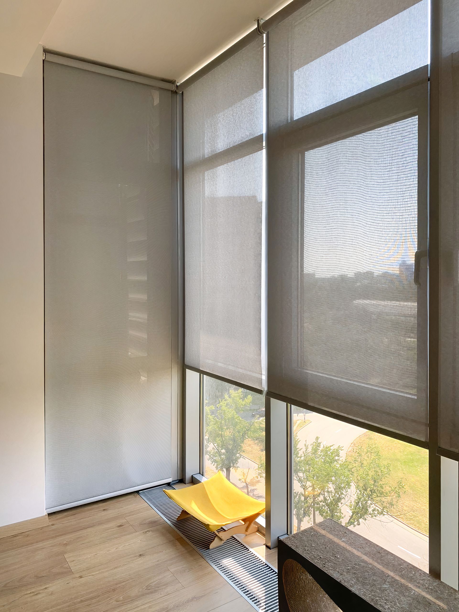 Sunlit balcony with gray roller shades and a yellow folding chair by the window