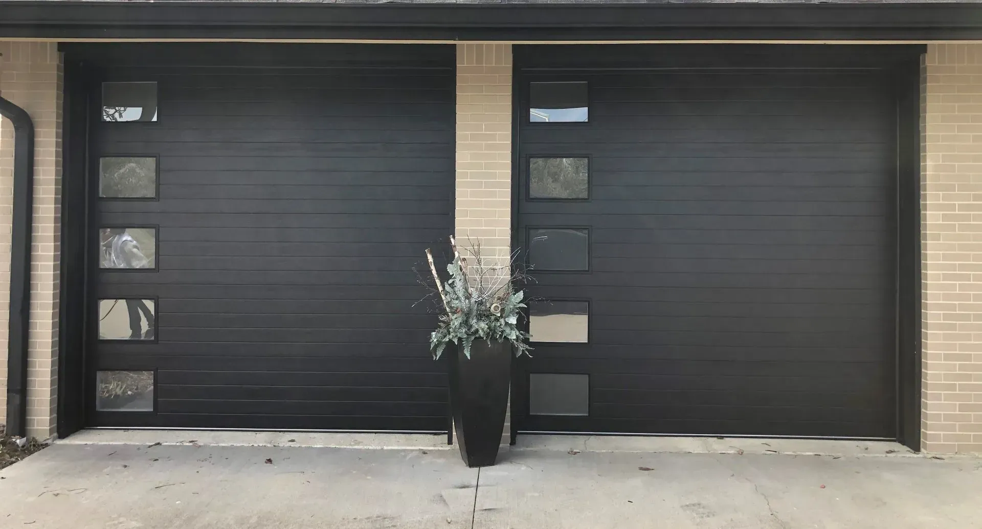 Two black garage doors with a potted floral arrangement centered between them