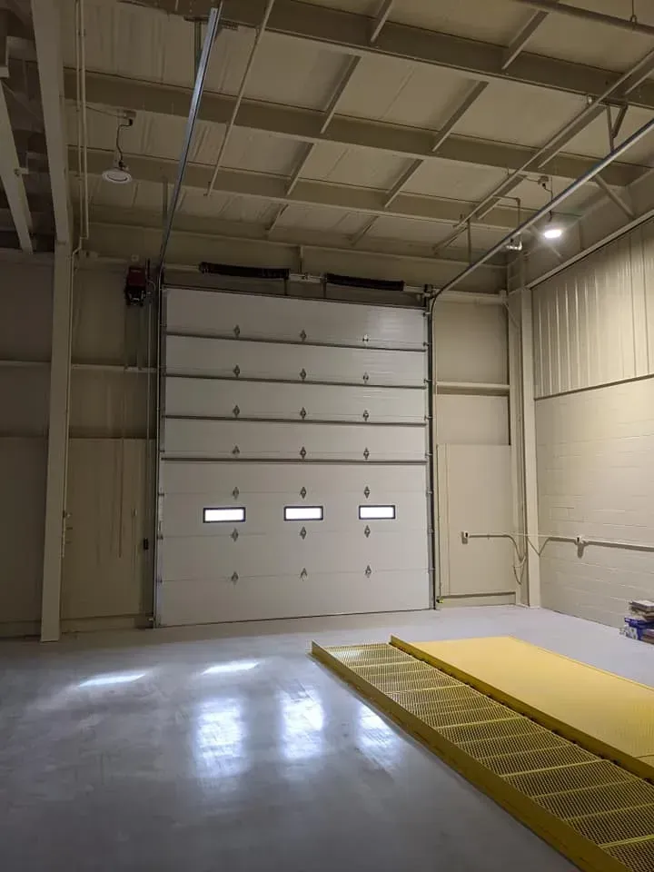 Empty warehouse interior with a large white roll-up door and yellow safety mat on the floor.