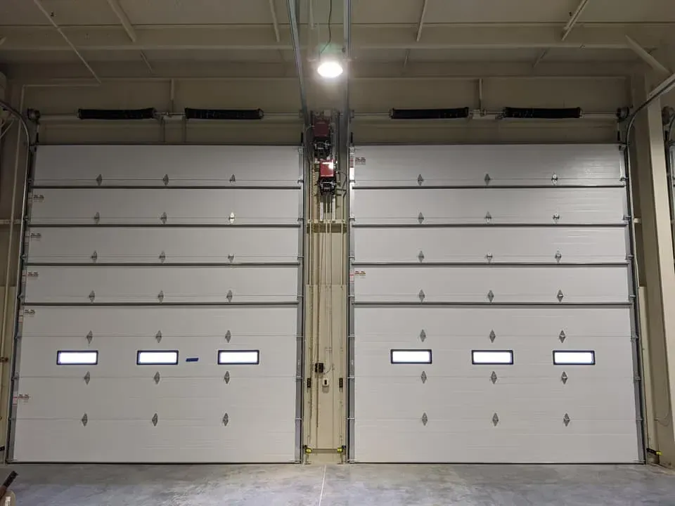Two white garage doors in an industrial building, with small windows and overhead tracks.