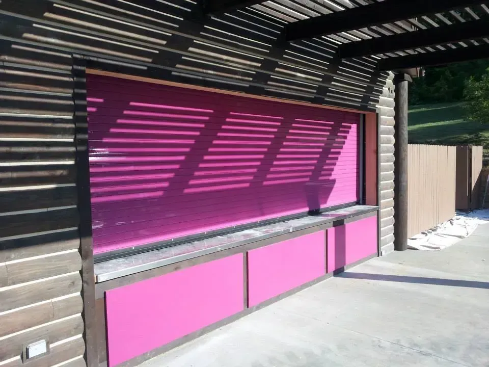 Pink storefront with striped awning and closed service window in bright sunlight