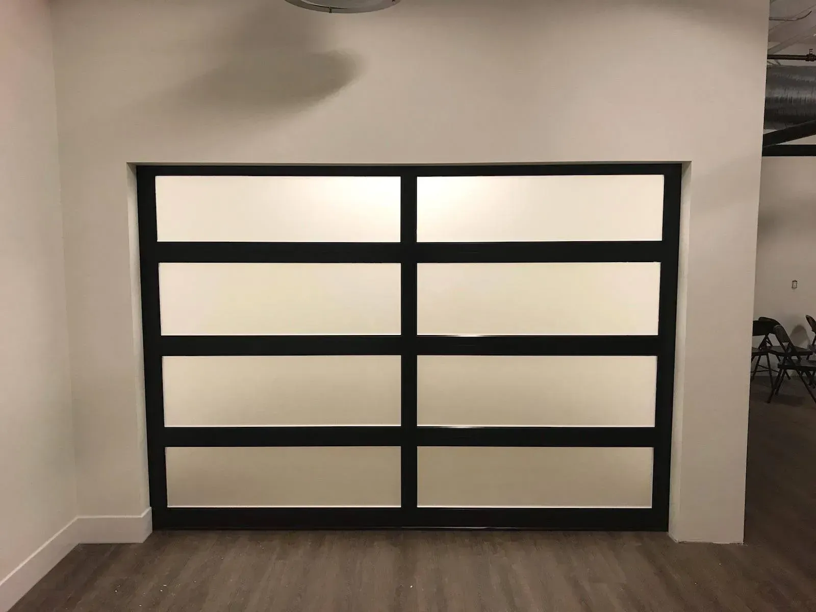 Black-framed glass garage door centered in a beige hallway-like interior.