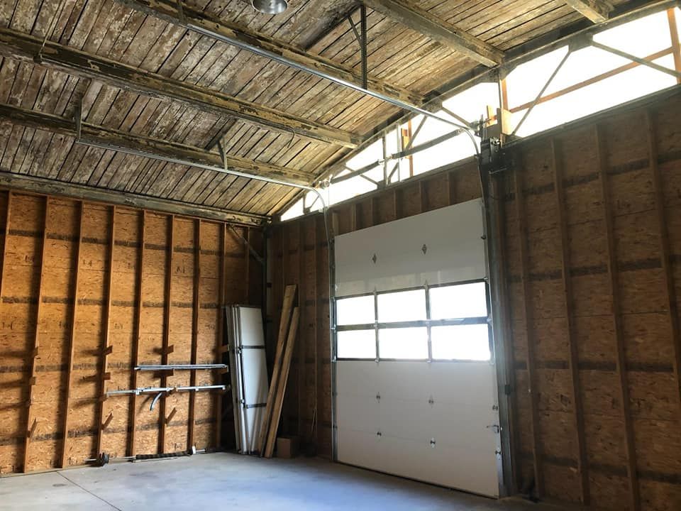 Empty unfinished garage interior with exposed wood framing and a white roll-up door
