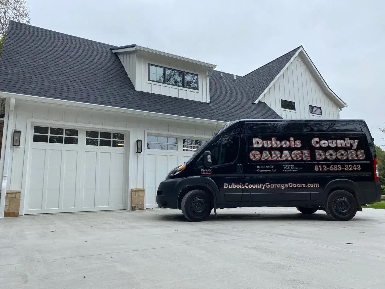 Black service van parked in front of a white house with double garage doors.