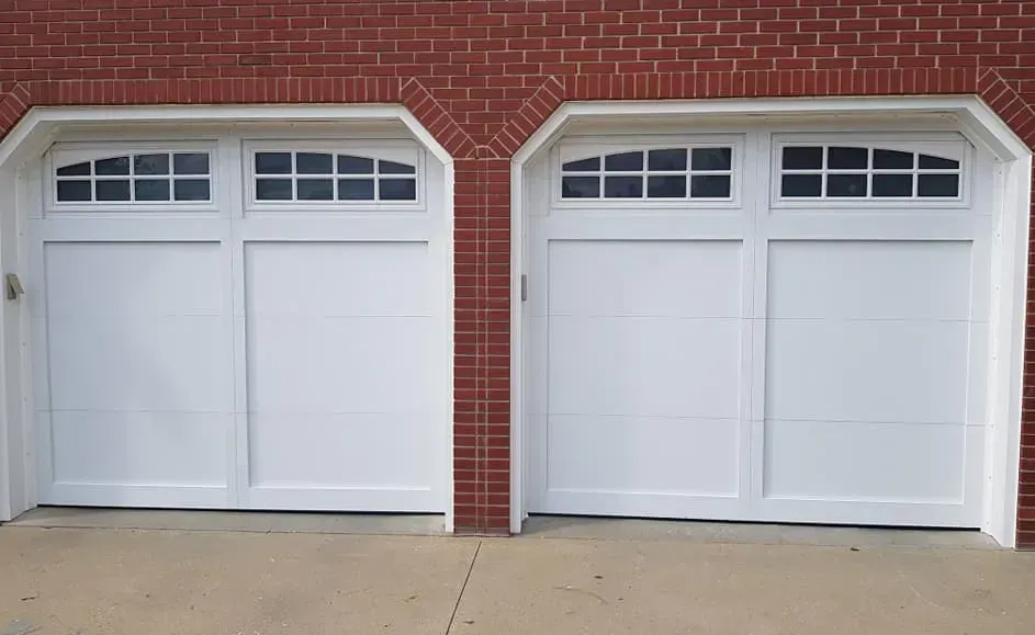 Two white garage doors with arched windows on a red brick house