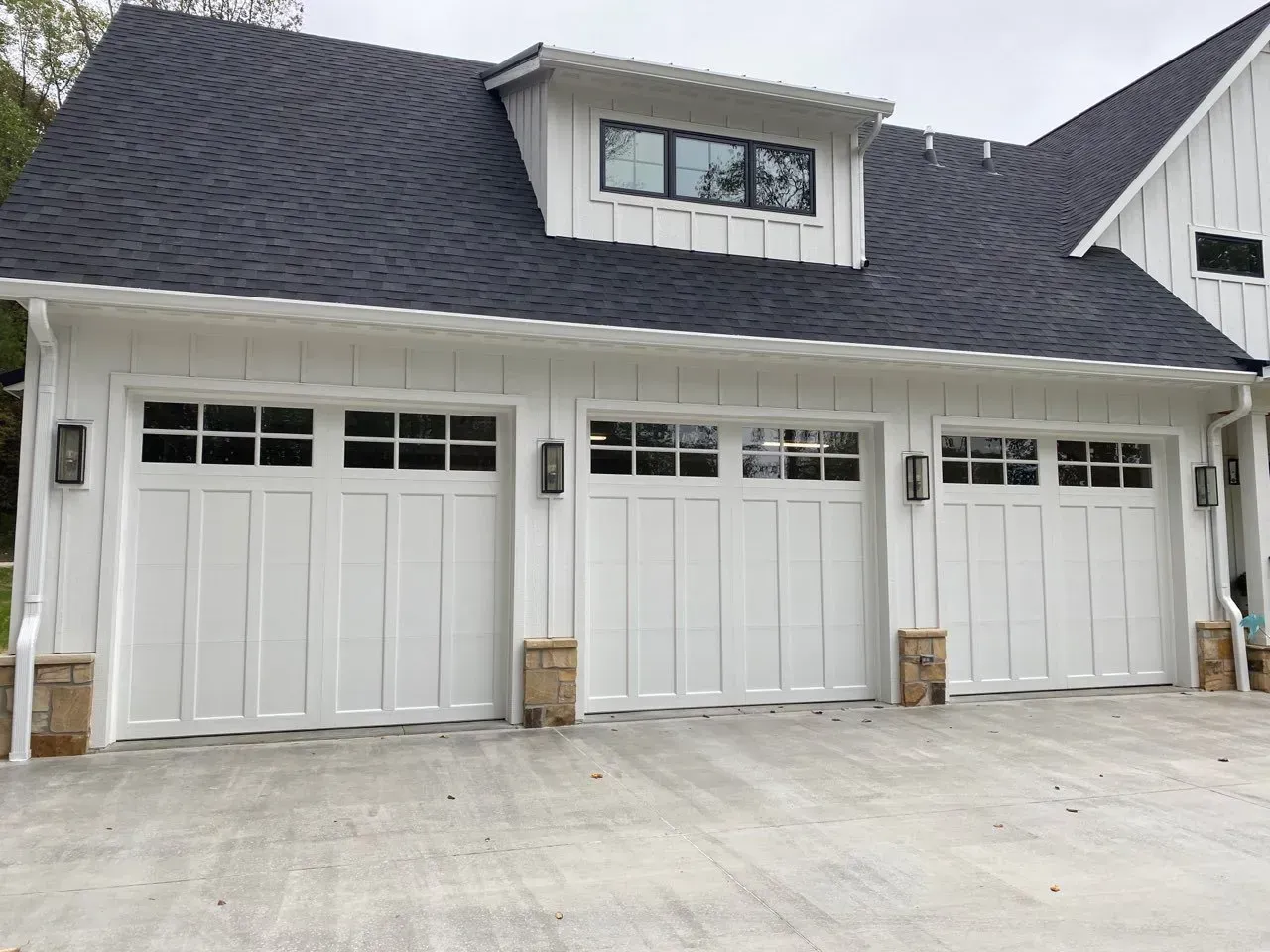 White three-car garage with black roof and dormer window, viewed from the driveway