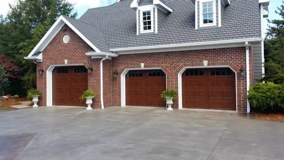 Brick house with three wooden garage doors and a wide concrete driveway
