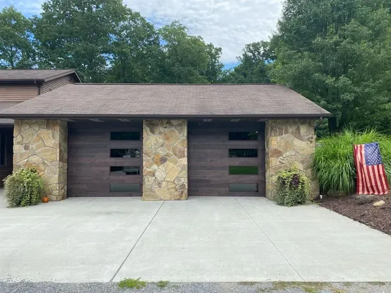 Stone-front two-car garage with dark brown doors and a U.S. flag by the driveway