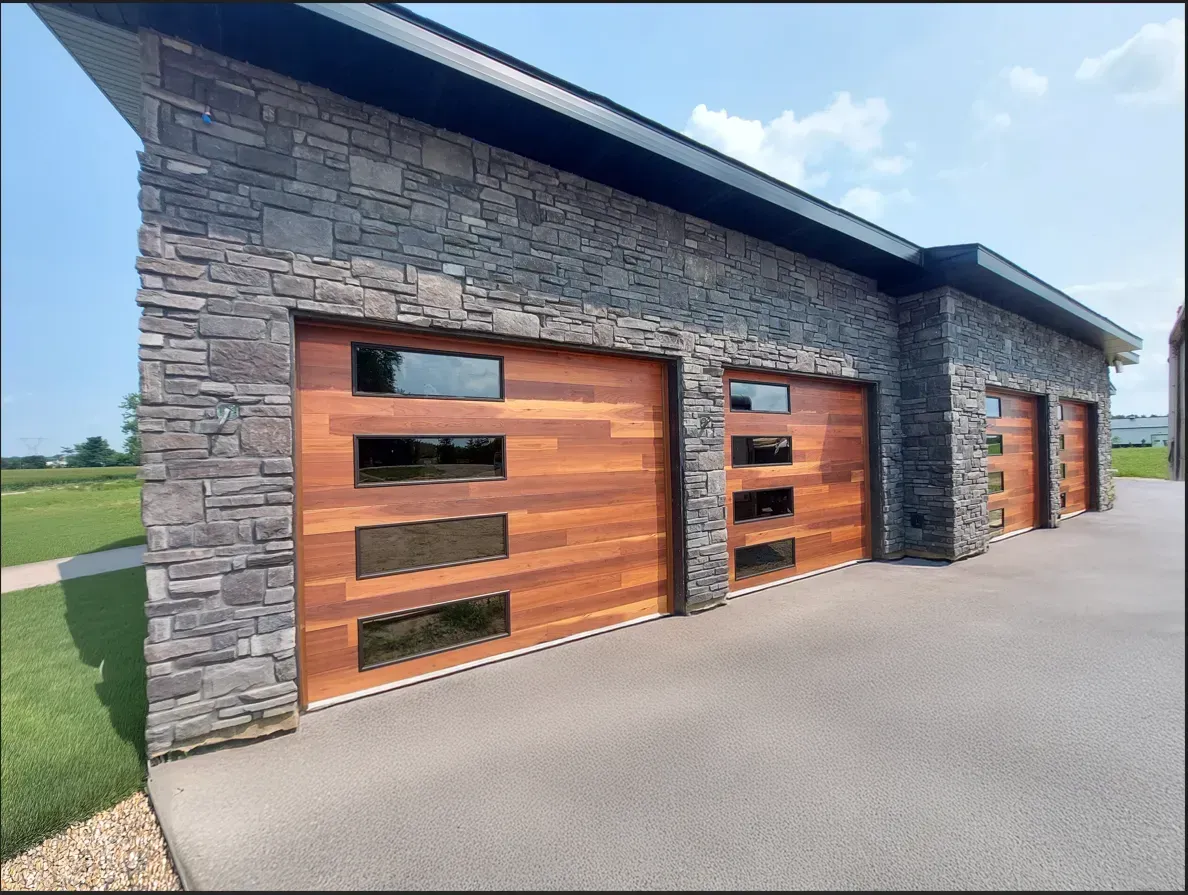 Modern stone building with wood garage doors along a paved driveway under a blue sky
