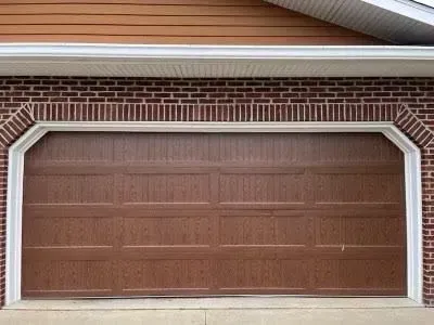 Brown double garage door with white trim on a brick house