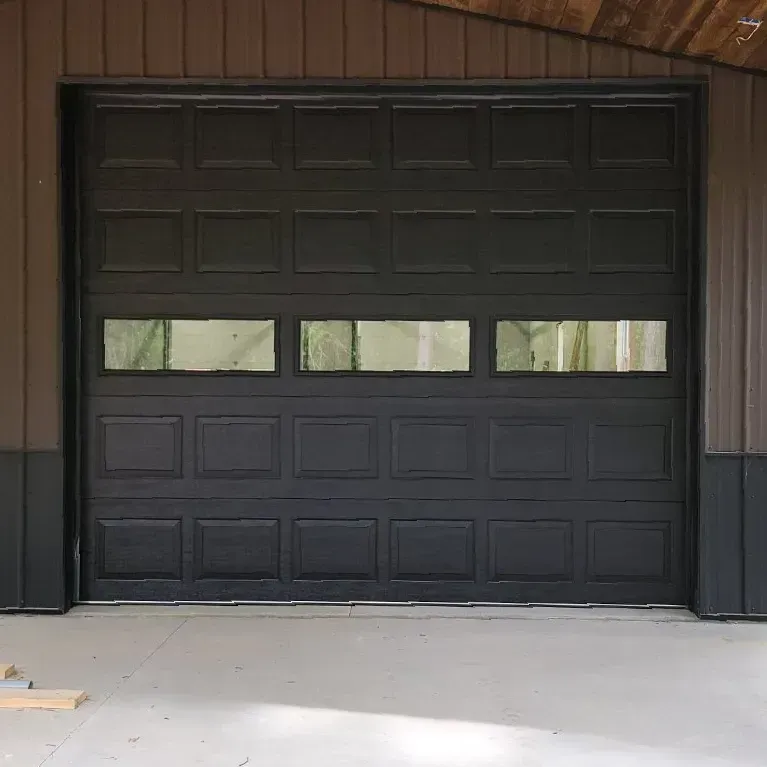 Black garage door with three narrow windows set in a brown building facade
