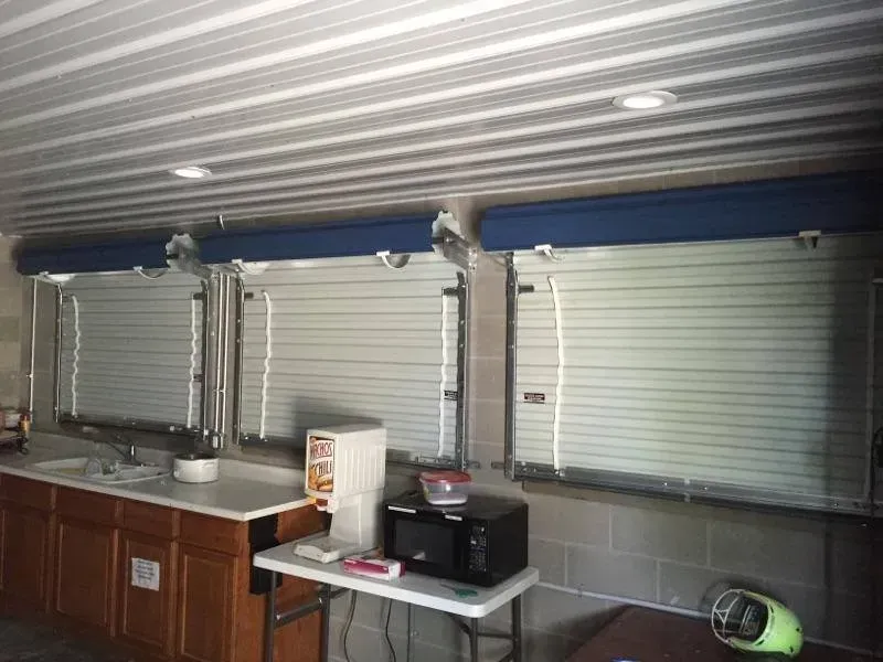 Kitchen with closed metal window shutters, blue trim, sink, counter, and microwave on a table