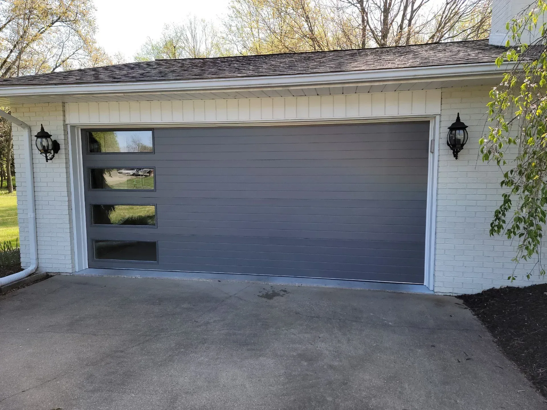 White brick house with a gray garage door and driveway, viewed from the front