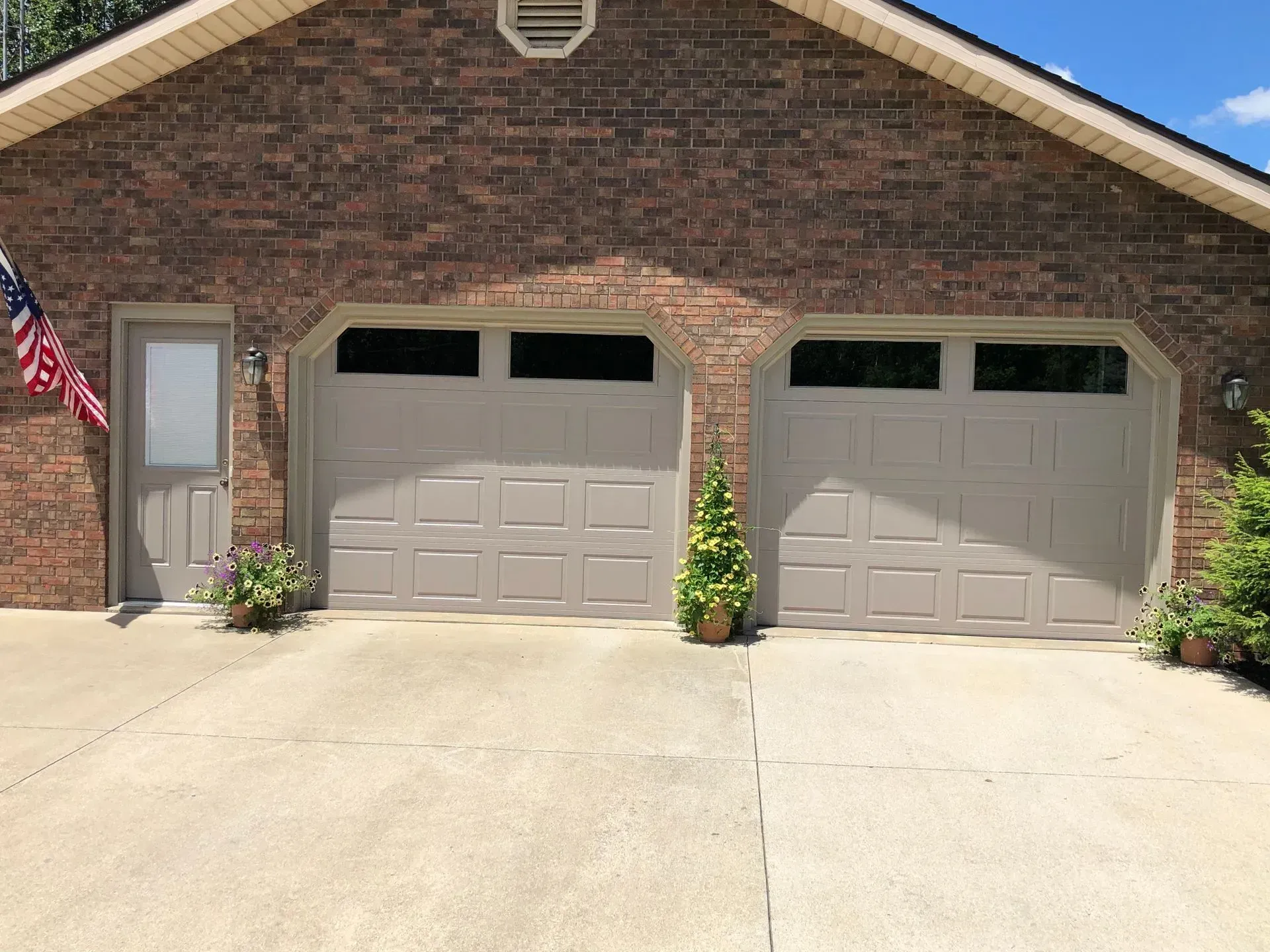 Brick house with two beige garage doors and a wide concrete driveway.