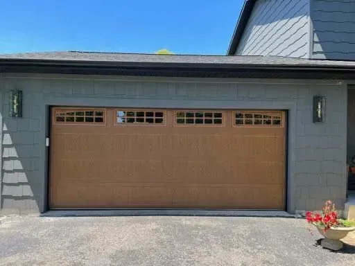 Suburban house exterior with a tan double garage door and gray siding under a blue sky
