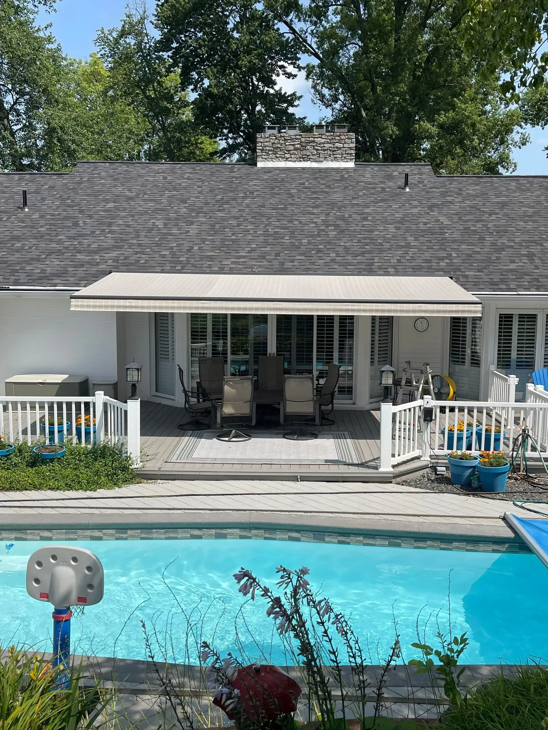 Backyard pool and patio with lounge chairs, white railings, and house behind it