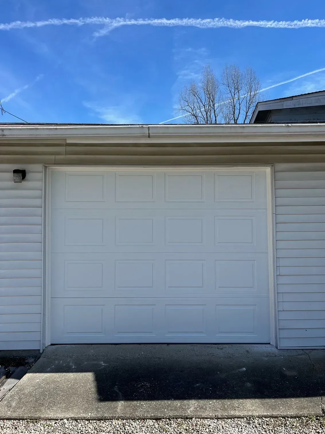 White garage door on a house exterior with siding, driveway, and blue sky above