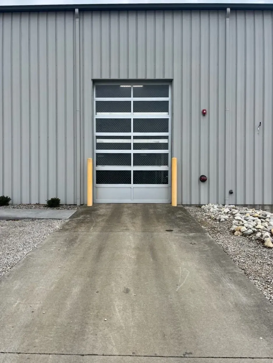 Industrial building entrance with a glass garage door, concrete ramp, and gravel sides
