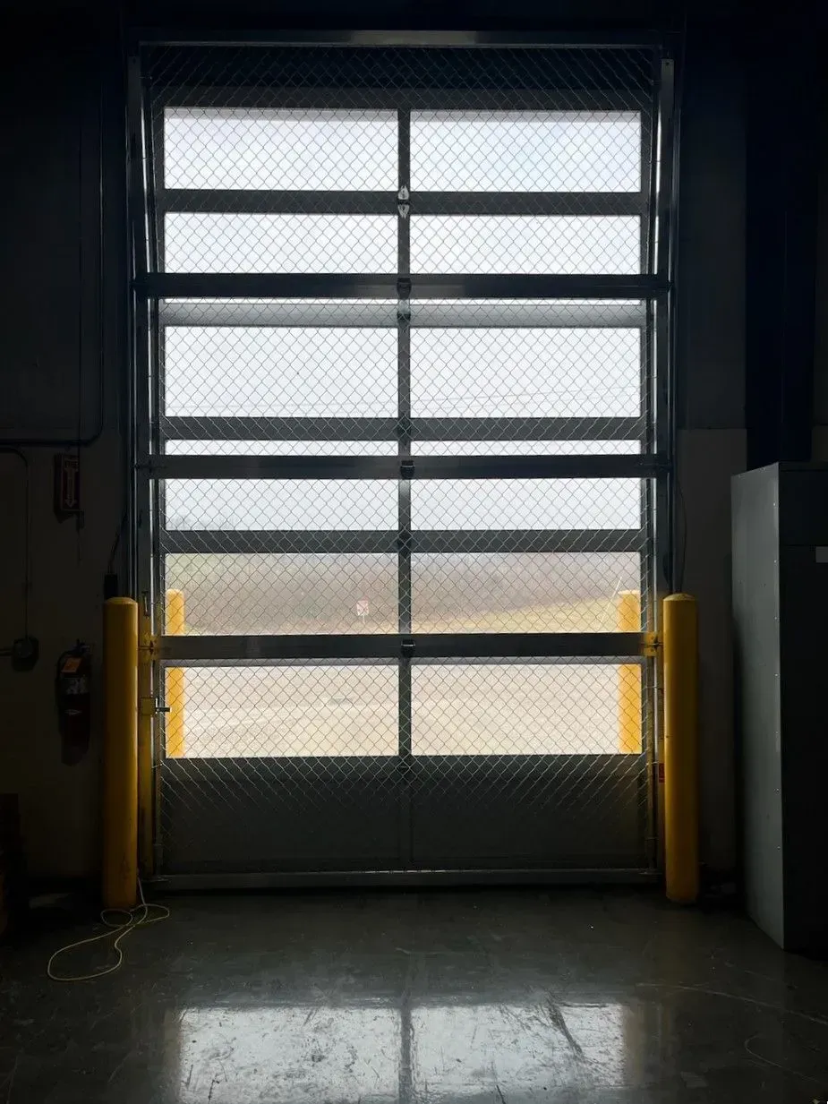 Closed metal garage door with windows and bright daylight beyond, viewed from a dim warehouse interior