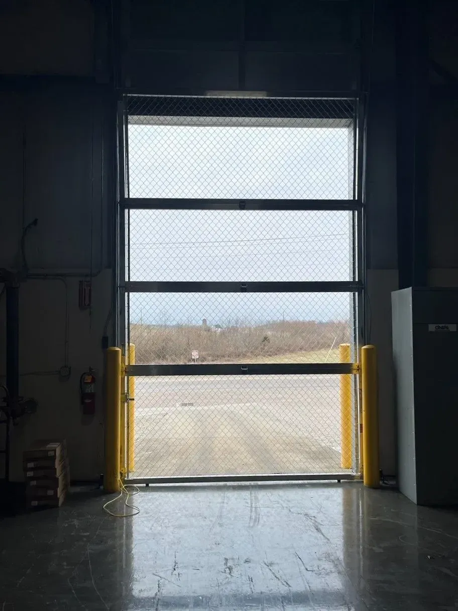 Interior view of a warehouse bay door with bright daylight and a yellow barrier at the bottom