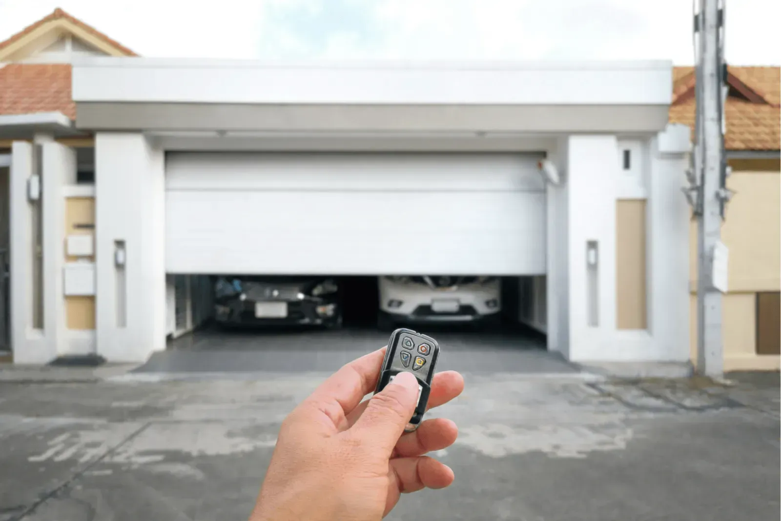 Hand holding a garage remote pointed at a white double garage door with cars inside