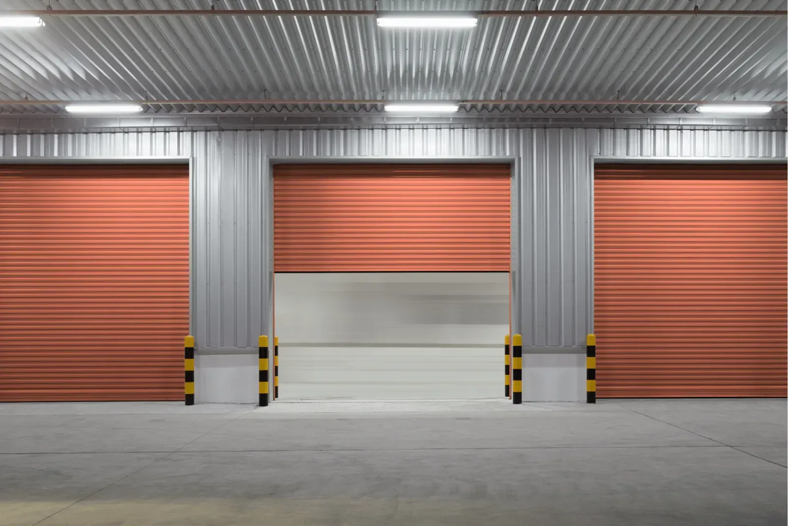 Industrial warehouse with three orange roll-up doors and gray metal siding