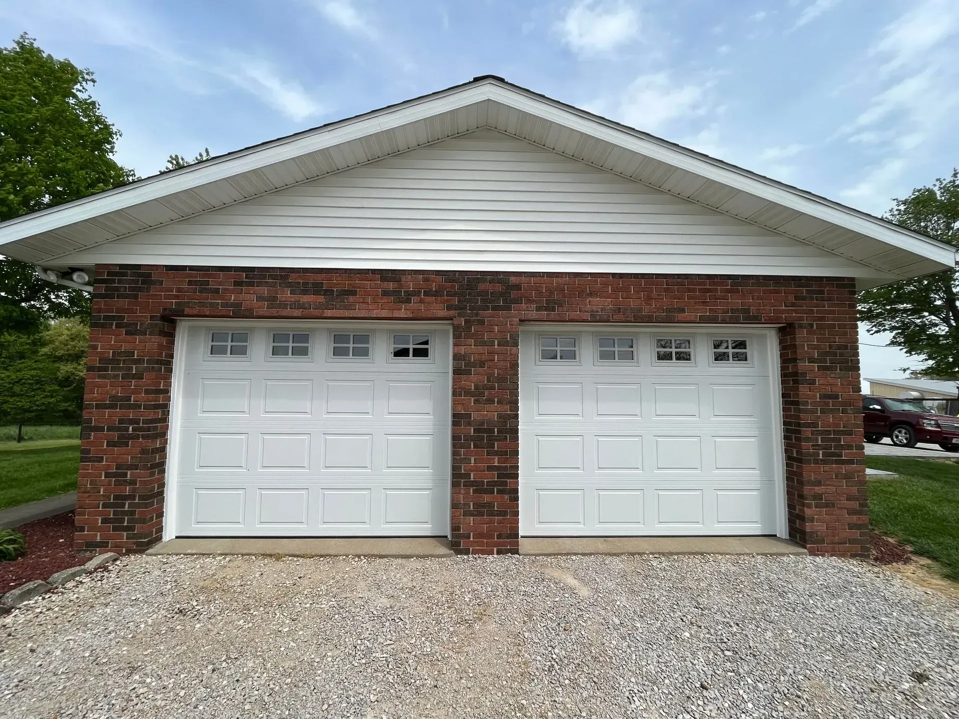 Two-car brick garage with white doors and gravel driveway